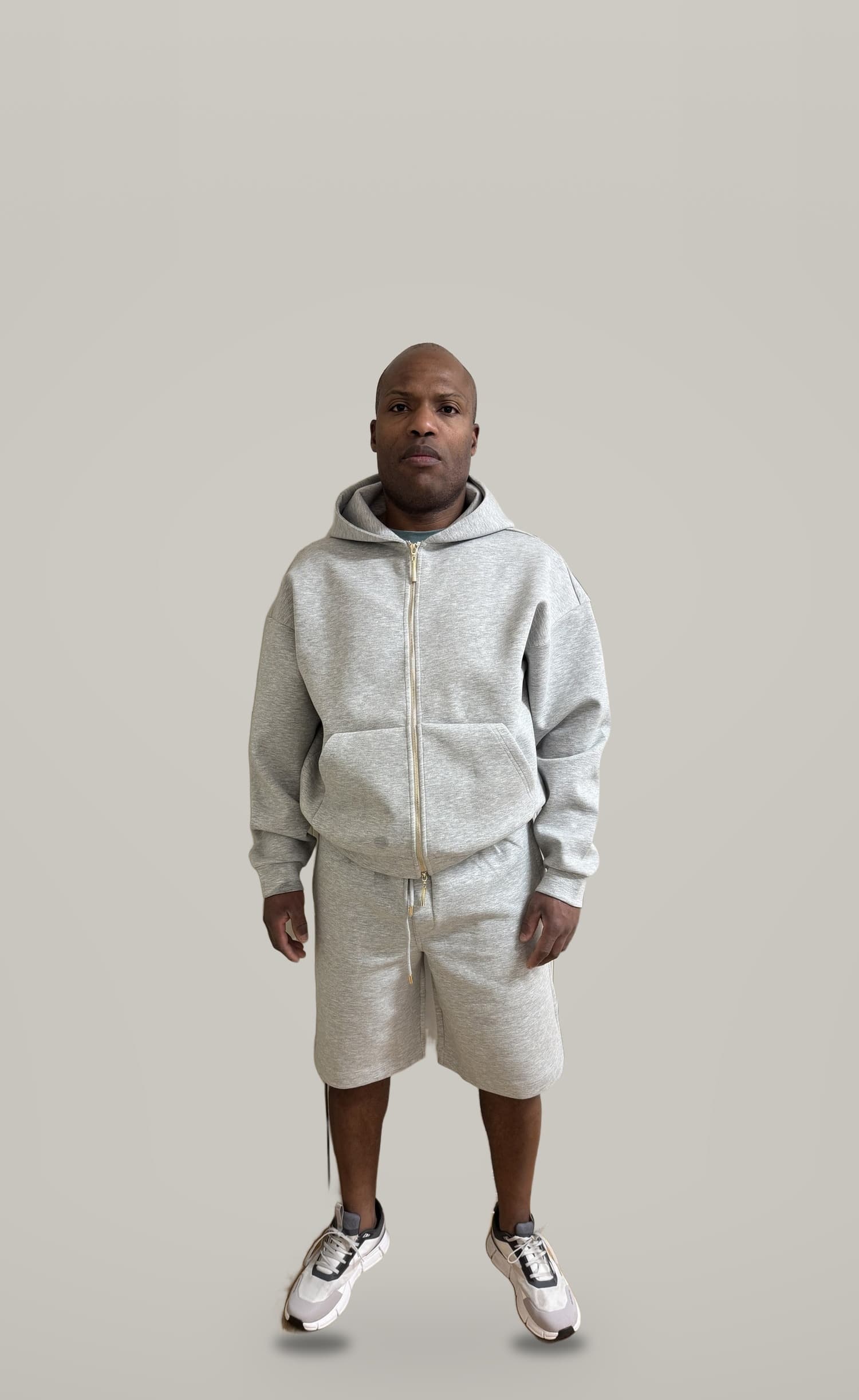 A model wearing the Chelsea Zip Hoodie and Chelsea Shorts in grey marl against a plain studio backdrop
