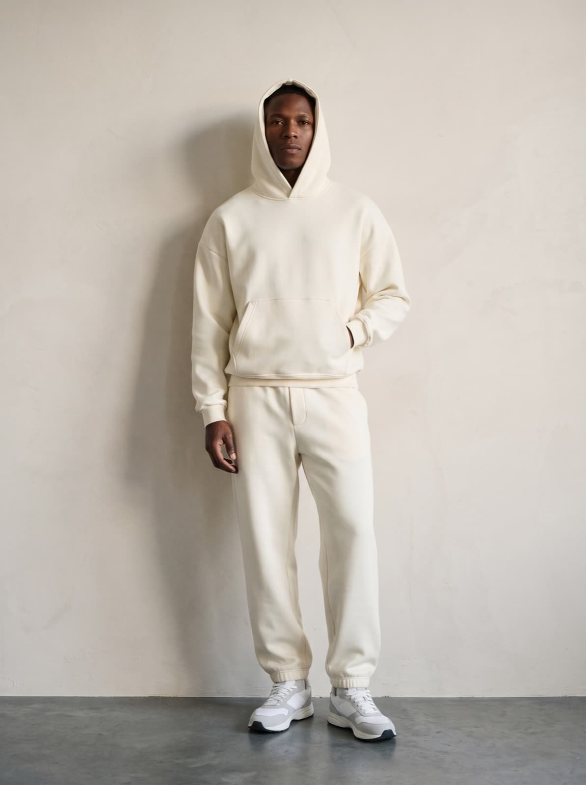 A model wearing the Chelsea Pullover and joggers in cream, hood up